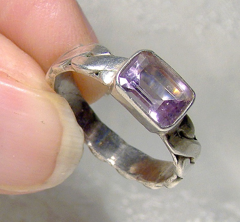 May include: A silver ring with a light purple gemstone. The ring has a braided design.