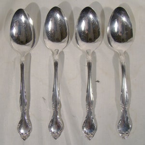 May include: Four silver spoons with ornate handles. The spoons are polished and shiny.