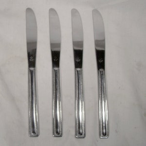 May include: Four silver dinner knives with a beaded pattern on the handle. The knives have a simple, elegant design.