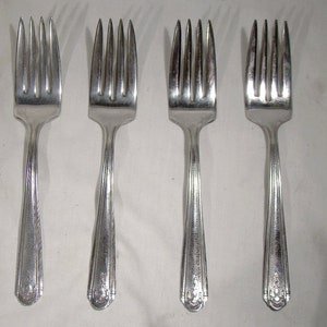 May include: Four silver forks with tines and decorative handles. The forks are arranged in a row, showcasing their polished finish and intricate design. A classic set for dining.