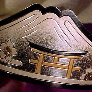 Pu&ograve; includere: Un braccialetto d'argento con una scena di montagna giapponese e un torii. Il braccialetto &egrave; decorato con fiori di ciliegio e ha un design in bianco e nero.