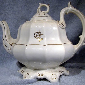 May include: White teapot with a gold floral design and a scalloped base. The teapot has a fluted body and a decorative handle.