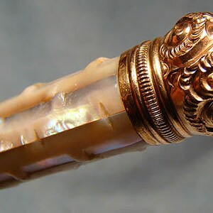 May include: A decorative bottle stopper with a gold-toned metal cap and a mother-of-pearl body.