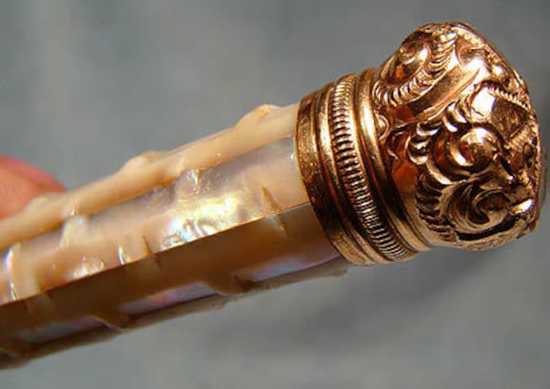 May include: A decorative bottle stopper with a gold-toned metal cap and a mother-of-pearl body.