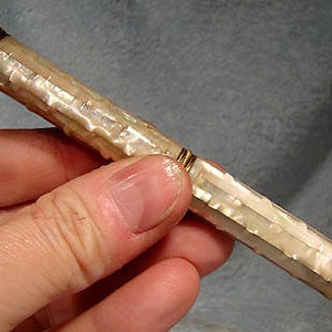 May include: A white mother-of-pearl pen with gold accents. The pen has a ribbed design and is approximately 6 inches long.