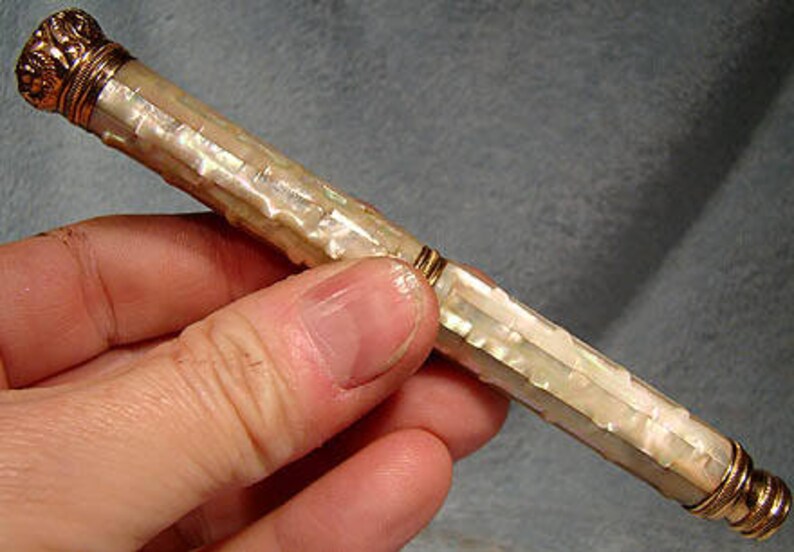 May include: A white mother-of-pearl pen with gold accents. The pen has a ribbed design and is approximately 6 inches long.