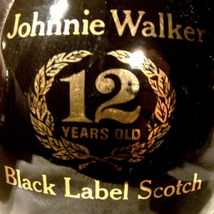 May include: A black bottle with gold lettering that reads "Johnnie Walker Black Label Scotch 12 Years Old". The bottle has a gold laurel wreath with the number "12" in the center.