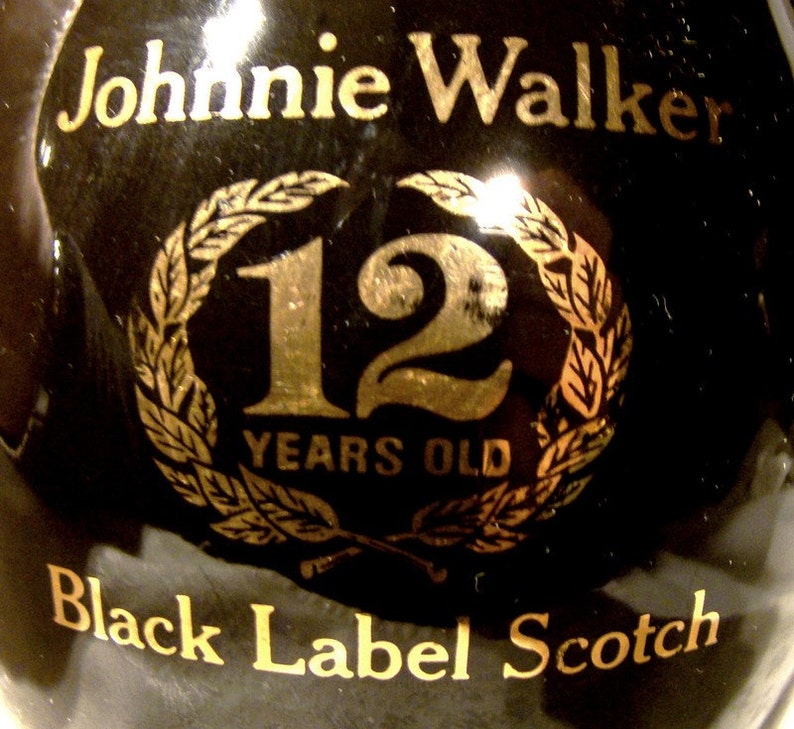May include: A black bottle with gold lettering that reads "Johnnie Walker Black Label Scotch 12 Years Old". The bottle has a gold laurel wreath with the number "12" in the center.