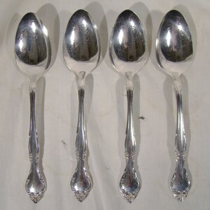 May include: Four silver spoons with ornate handles. The spoons are polished and shiny.