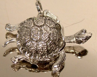 May include: A silver turtle pendant with a detailed shell and limbs. The pendant has a loop for a chain and is designed with a textured shell pattern. The turtle's head and legs are extended, giving it a lifelike appearance.