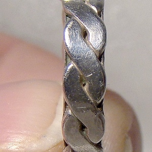 May include: A silver ring with a braided design. The ring is made of a smooth, polished metal.