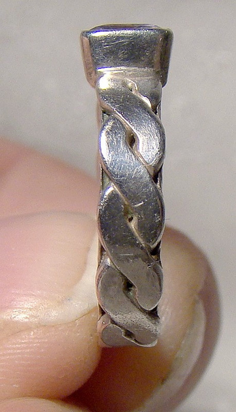 May include: A silver ring with a braided design. The ring is made of a smooth, polished metal.