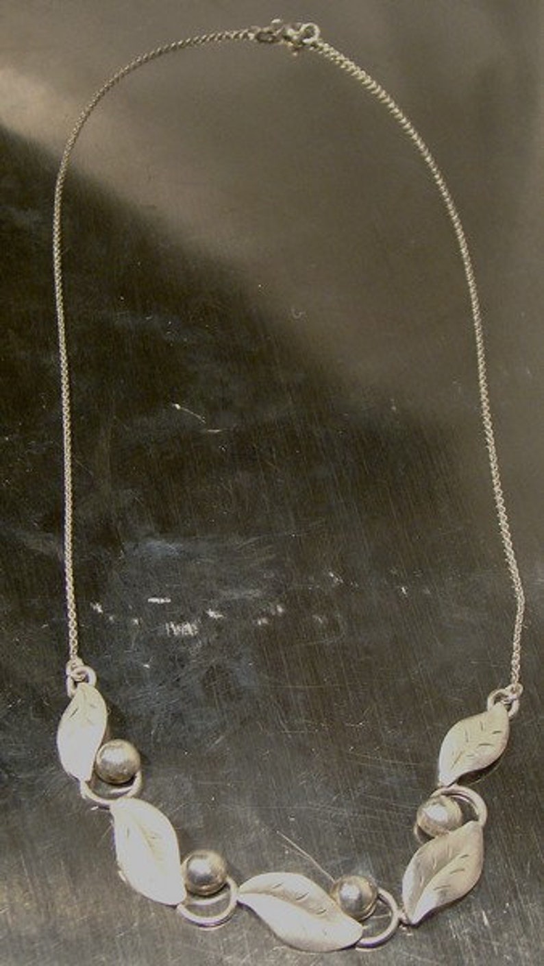 K&ouml;nnte beinhalten: Eine silberne Halskette mit einer zarten Kette und einem Anh&auml;nger aus Bl&auml;ttern und runden Perlen.