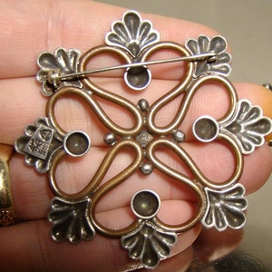 May include: A silver and copper brooch with a floral design and five round stones. The brooch has a pin on the back.