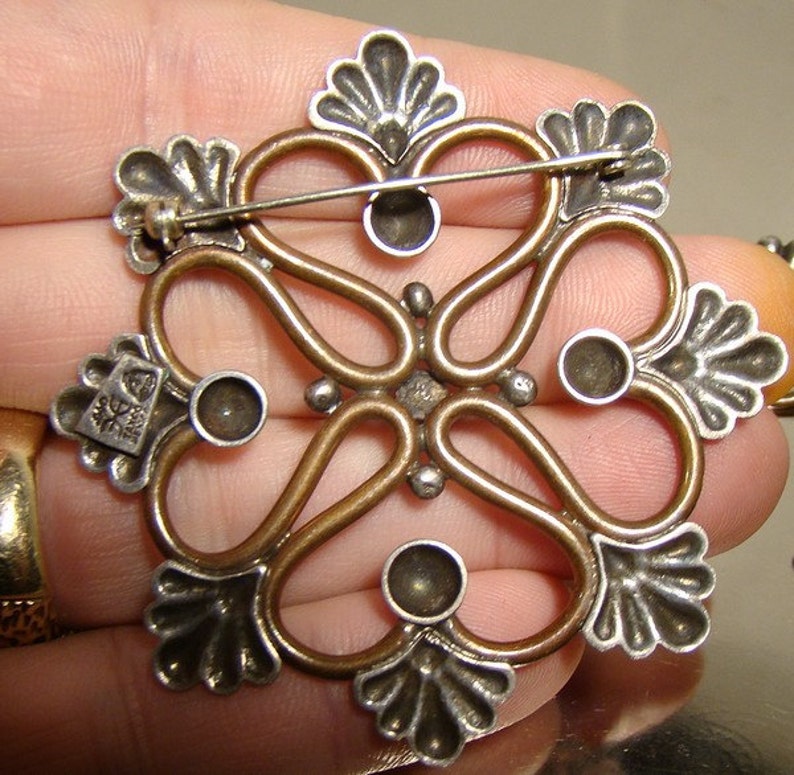 May include: A silver and copper brooch with a floral design and five round stones. The brooch has a pin on the back.