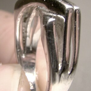 May include: A silver ring with a unique, open design. The ring is made of polished metal and has a smooth, rounded surface.