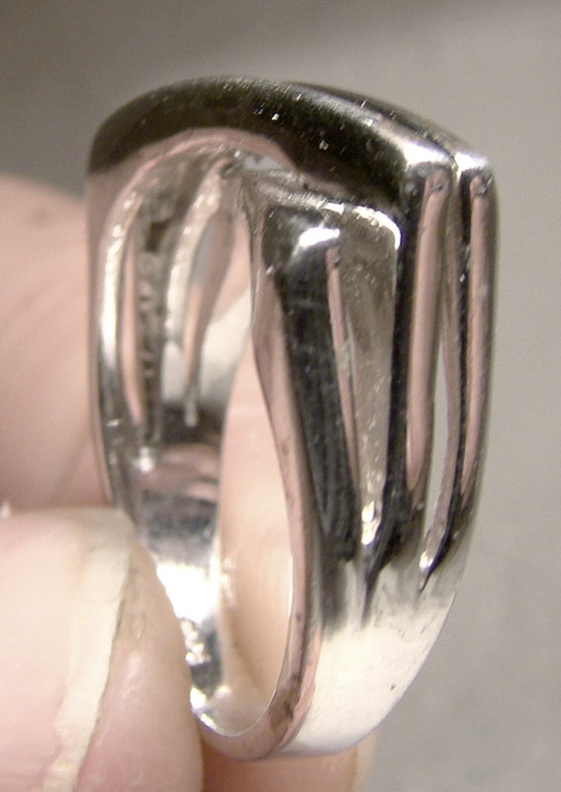May include: A silver ring with a unique, open design. The ring is made of polished metal and has a smooth, rounded surface.