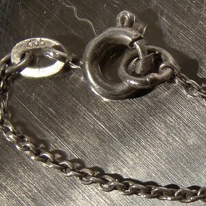 K&ouml;nnte beinhalten: Eine silberne Kettenkette mit einem Karabinerverschluss. Die Kette besteht aus kleinen, runden Gliedern.