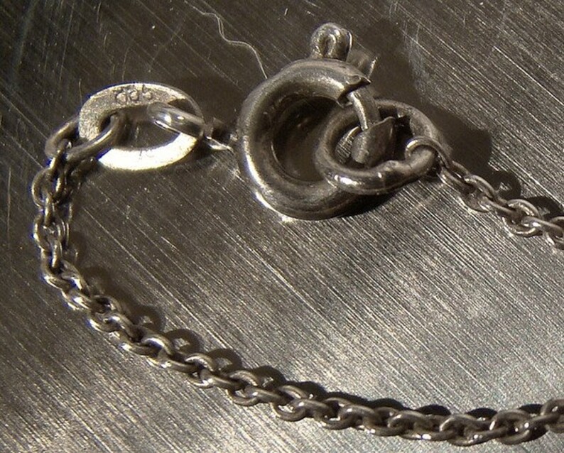 K&ouml;nnte beinhalten: Eine silberne Kettenkette mit einem Karabinerverschluss. Die Kette besteht aus kleinen, runden Gliedern.