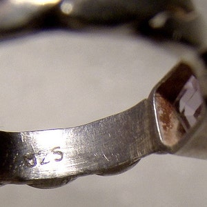 May include: Close-up of the inside of a silver ring with a clear stone set in the band. The ring is marked with the number "925" on the inside of the band.