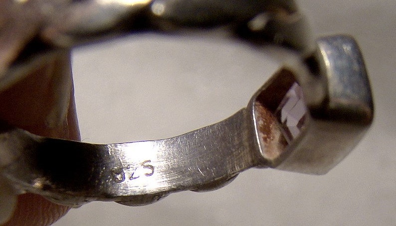 May include: Close-up of the inside of a silver ring with a clear stone set in the band. The ring is marked with the number "925" on the inside of the band.