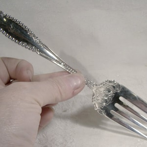 May include: A silver fork with an ornate handle and a decorative design. The fork has three tines.