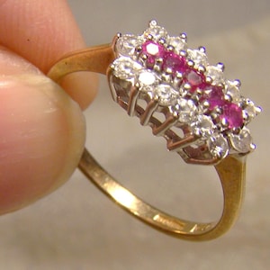 May include: A gold ring featuring a cluster of small diamonds and pink rubies set in a floral design.