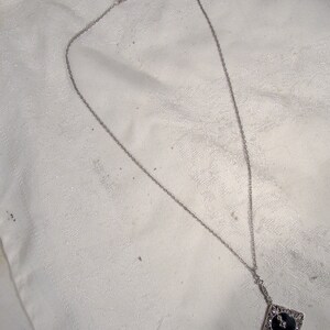May include: A silver chain necklace with a black and silver pendant. The pendant is a square with a black stone in the center and silver filigree around the edges.