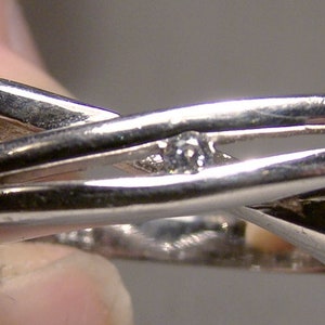 May include: A silver ring with a criss-cross design and a single small diamond set in the centre.
