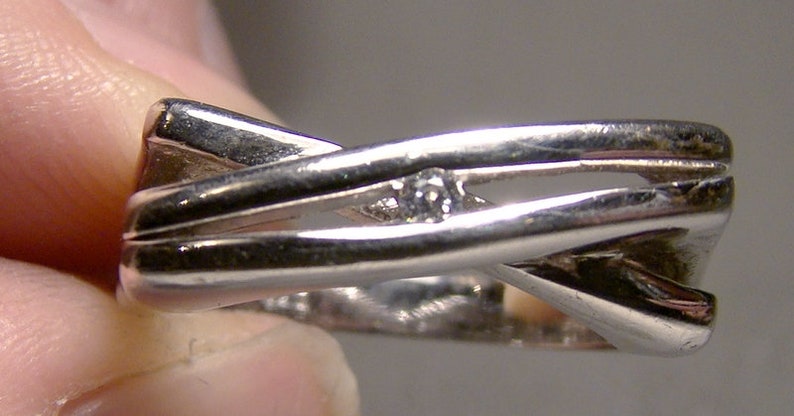 May include: A silver ring with a criss-cross design and a single small diamond set in the centre.