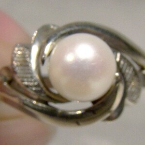 May include: A silver ring with a large, white pearl set in a swirling design.