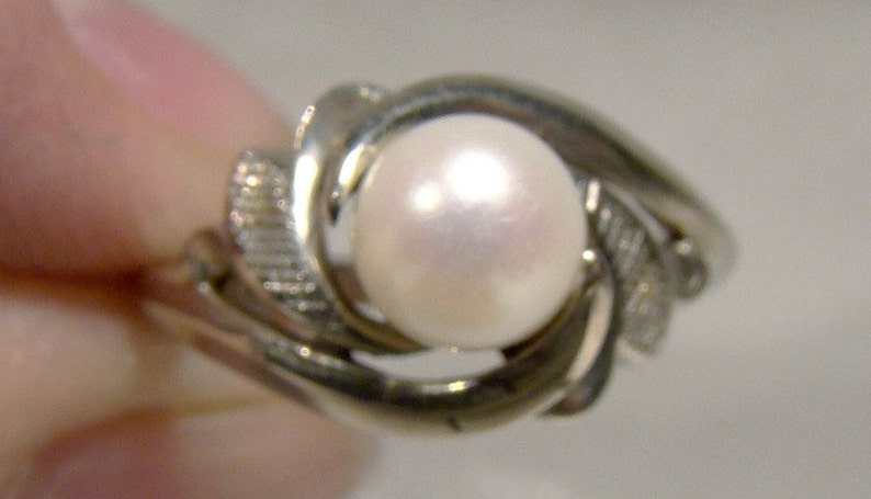 May include: A silver ring with a large, white pearl set in a swirling design.