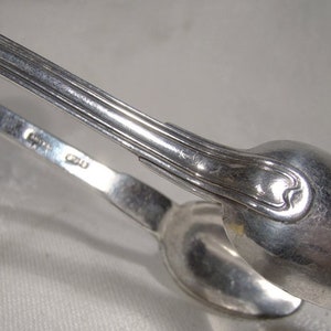 Puede incluir: Pinzas de az&uacute;car de plata con un dise&ntilde;o decorativo en el mango. Las pinzas est&aacute;n marcadas con el n&uacute;mero "820".