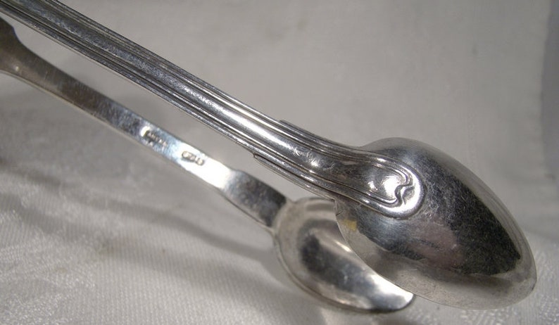 Puede incluir: Pinzas de az&uacute;car de plata con un dise&ntilde;o decorativo en el mango. Las pinzas est&aacute;n marcadas con el n&uacute;mero "820".