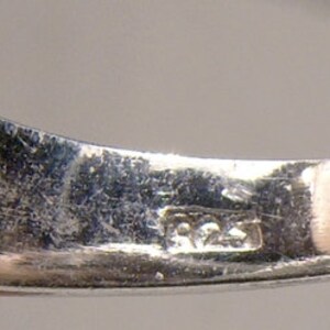 May include: Close-up of the inside of a silver ring with the inscription "925" on the band.