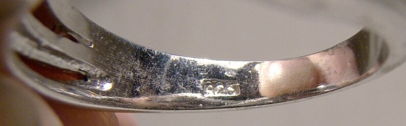 May include: Close-up of the inside of a silver ring with the inscription "925" on the band.