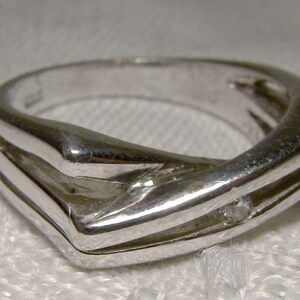 May include: A silver ring with a single diamond set in the centre. The ring has a unique, modern design with two bands that intersect.