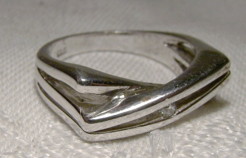 May include: A silver ring with a single diamond set in the centre. The ring has a unique, modern design with two bands that intersect.