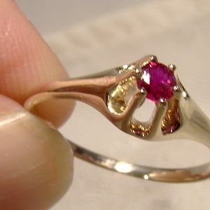 May include: A gold ring featuring a single, round, pink ruby gemstone set in a delicate, open-work design.