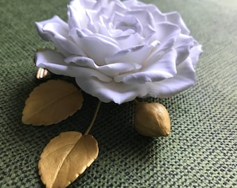 Rosa blanca con hojas, capullos y broche dorados.
