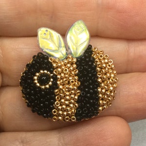 May include: A beaded bee brooch with black and gold beads. The bee has iridescent wings.