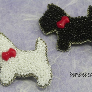 May include: Two beaded dog brooches, one black and one white, with red bows. The brooches are on a purple textured background with the text "Bumblebead".