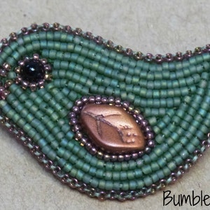 Op de afbeelding: Een groene kralen vogel broche met een koperkleurig bladontwerp. De vogel is gemaakt van kleine, ronde kralen en heeft een zwart oog.