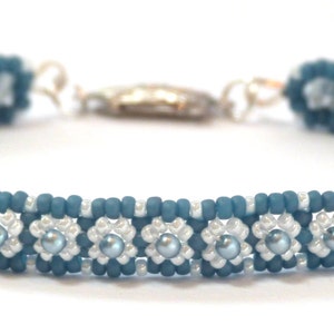 Puede incluir: Un brazalete de cuentas azules y plateadas con un diseño de flores. El brazalete está hecho con cuentas pequeñas y redondas y tiene un cierre plateado.