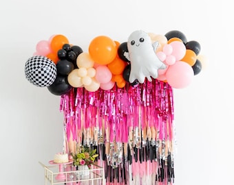 May include: A party decoration set featuring a balloon arch with orange, black, pink, and white balloons, including a checkered pattern balloon and a ghost-shaped foil balloon. A metallic pink and silver fringe curtain hangs below the balloons.