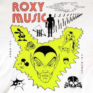 May include: A white t-shirt featuring a graphic print with the text ROXY MUSIC in red. The design includes a central yellow jagged shape containing a stylized face, surrounded by black line art illustrations of a skull, a cartoon mouse, and figures.
