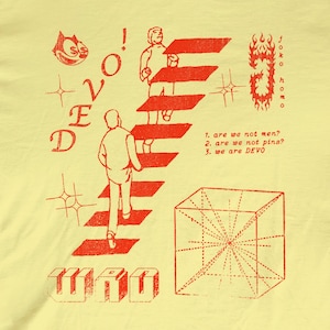 May include: A pale yellow t-shirt featuring a red graphic print of a person climbing stairs, a geometric cube, and the text DEVO, JOCKO HOMO, and a list: 1. are we not men? 2. are we not pins? 3. we are DEVO. The design includes a cartoon cat face.
