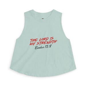 May include: A light blue sleeveless crop top with the text "THE LORD IS MY STRENGTH Exodus 15:8" in red and black. The top has a rounded neckline and a flared bottom hem.