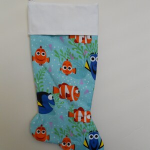 May include: A Christmas stocking featuring a light blue background with cartoon fish and seaweed. The stocking has a white cuff and a white hanging loop. The fish are orange, white, and blue.