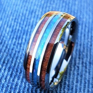 May include: A black tungsten carbide ring with a wood inlay and a blue opal inlay. The ring has a polished finish.